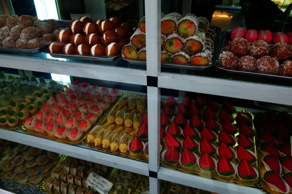 Trays of cakes and pastries on the shelves of a bakery window.