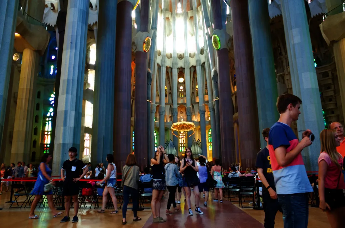 Visitors inside the Sagrada Família, among branching stone columns lit by coloured glass.