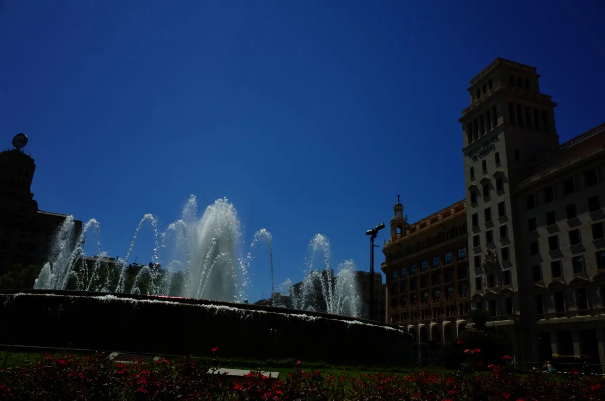 Fountains playing in a city square, with a tall stone building behind.