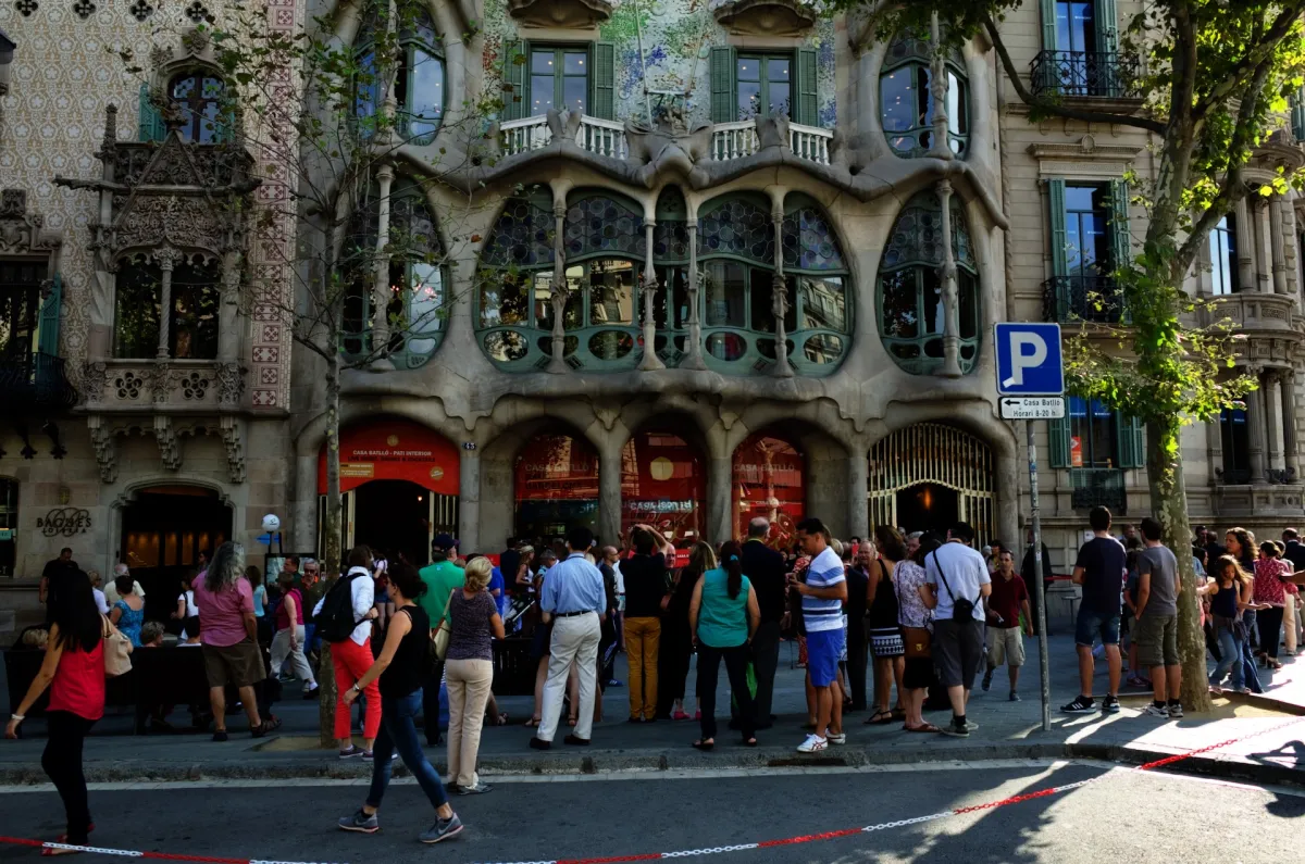 The curving stone and glass frontage of Casa Batlló, with a queue of people outside.
