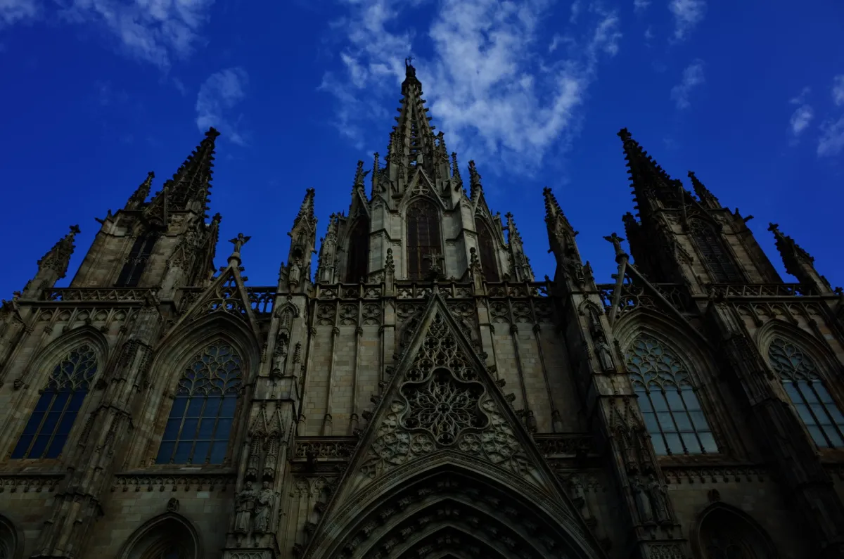 The gothic west front of Barcelona Cathedral seen from below against a dark blue sky.