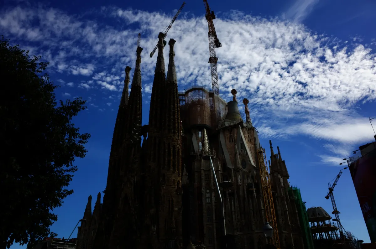 The Sagrada Família in silhouette against a deep blue sky with cranes alongside.