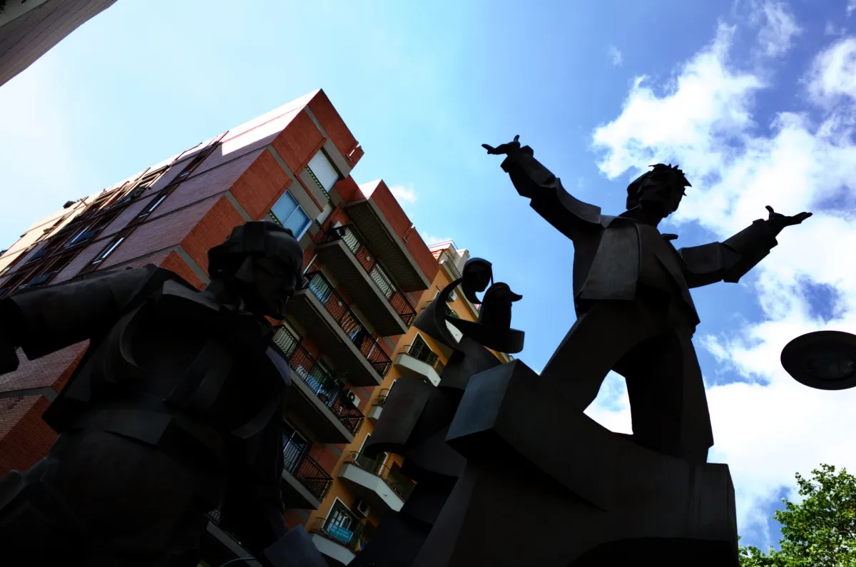 A bronze sculpture of figures with outstretched arms, seen from below against an apartment block.