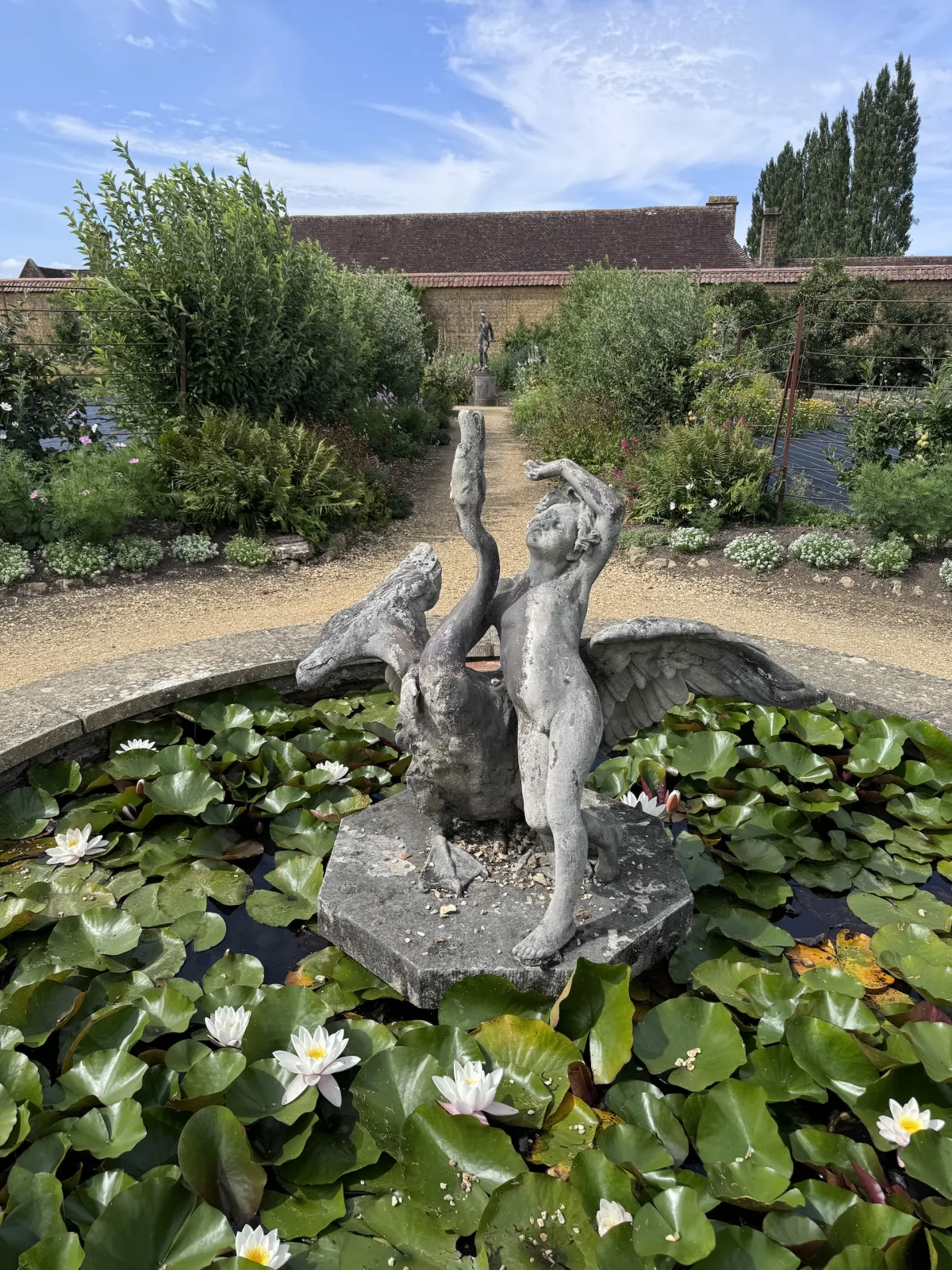 A stone fountain statue in a lily pond, with a walled garden behind.