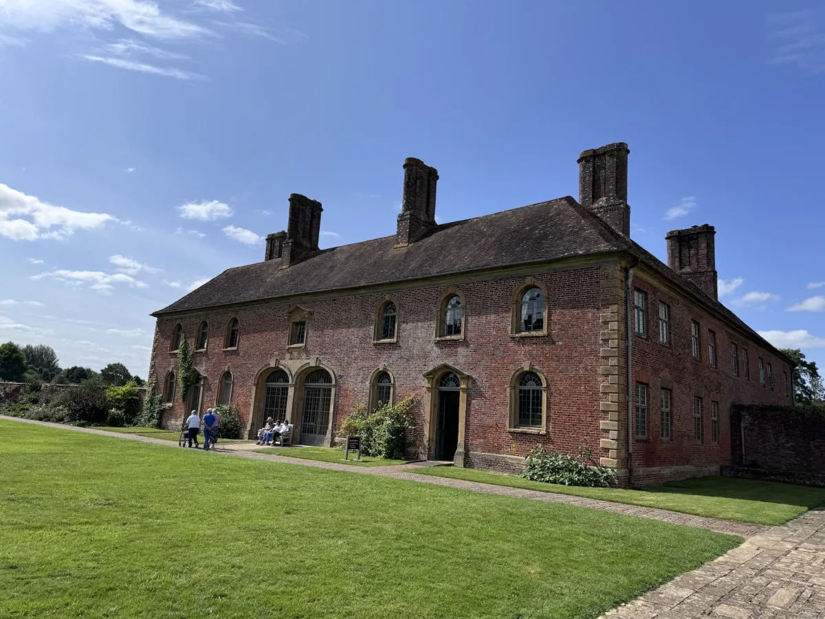 A long red brick range with tall chimneys, and visitors sitting outside.