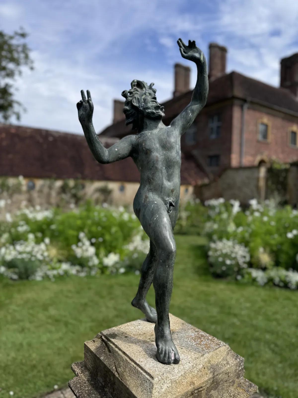 A bronze statue of a dancing figure on a stone plinth in a white garden.