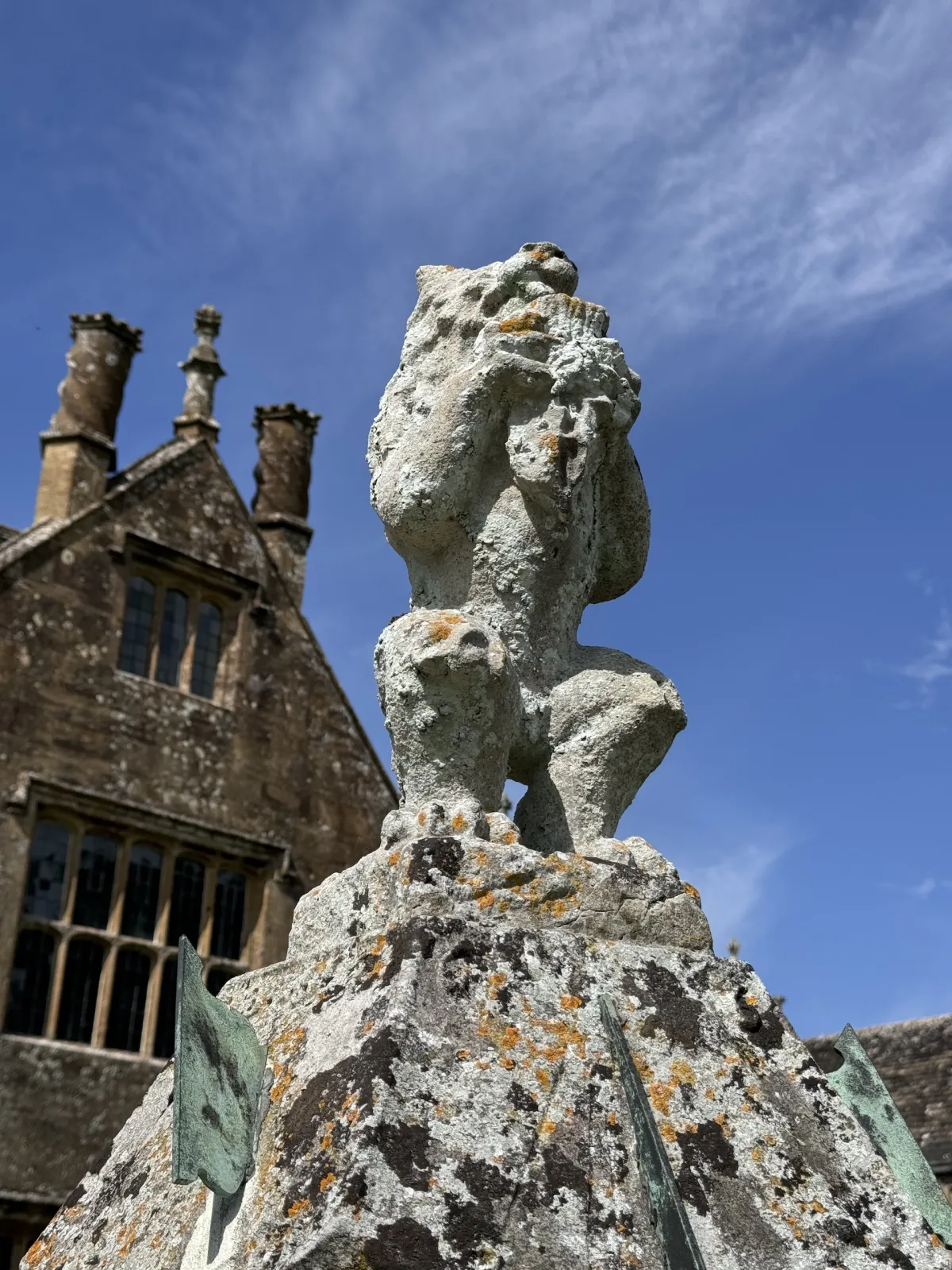 A weathered stone finial figure on a roof, against a blue sky.