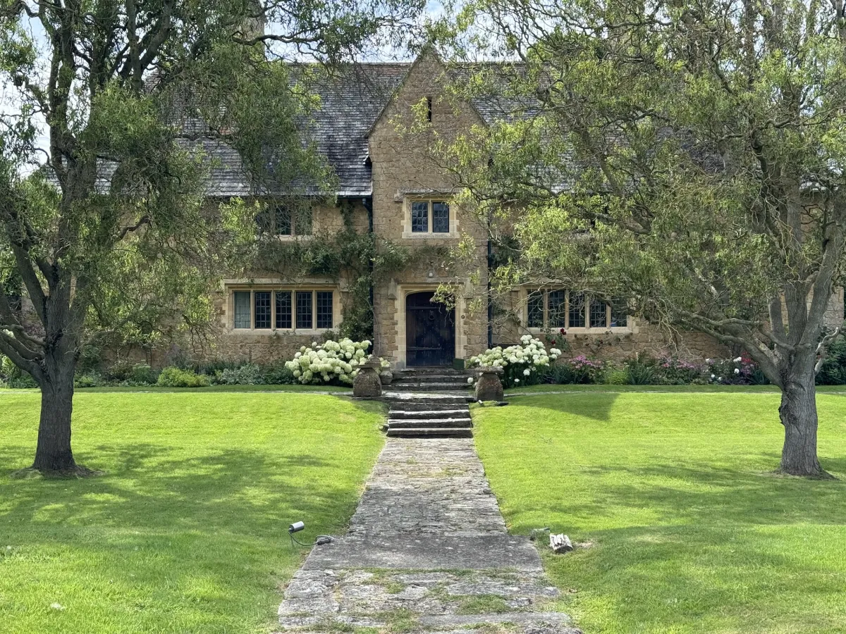 A stone house at the end of a path, framed by two trees.