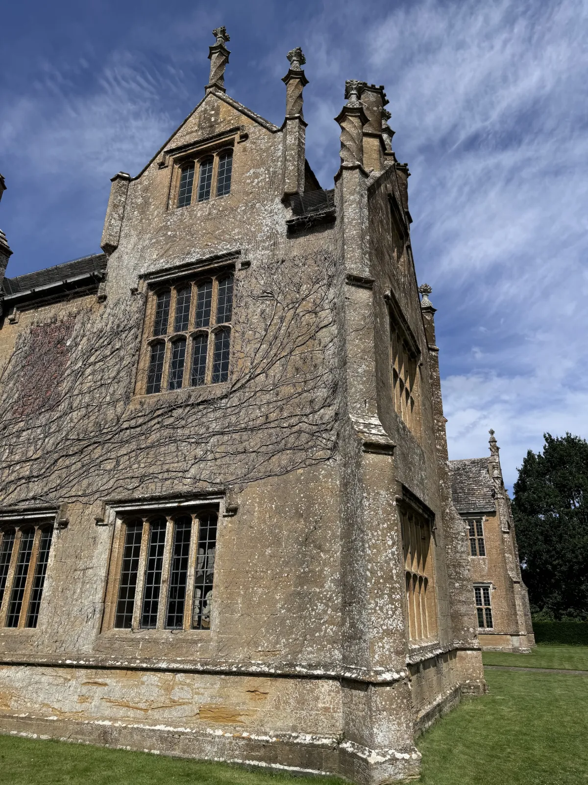 The gable end of a stone manor house with mullioned windows and finials.