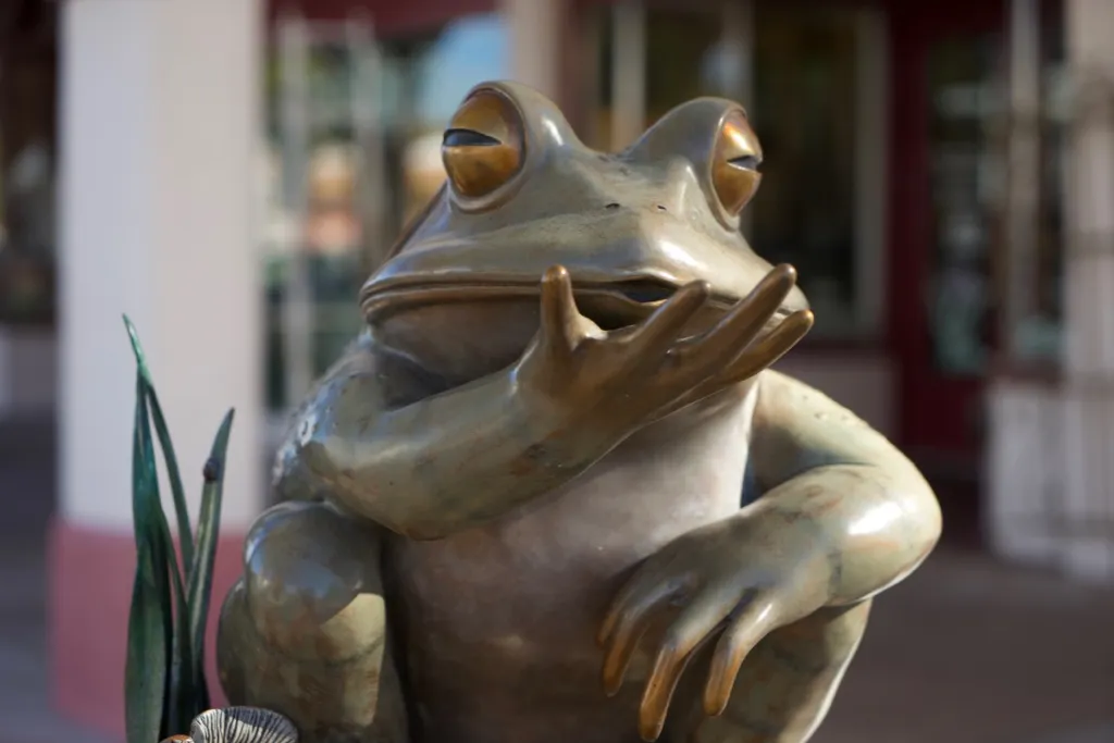 A bronze statue of a frog sitting with its arms folded on a shopfront pavement.