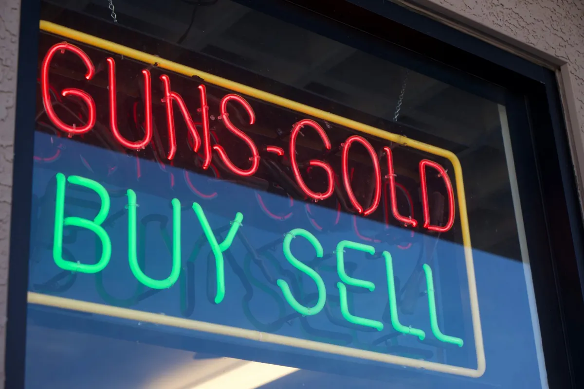A neon window sign reading Guns Gold in red above Buy Sell in green.