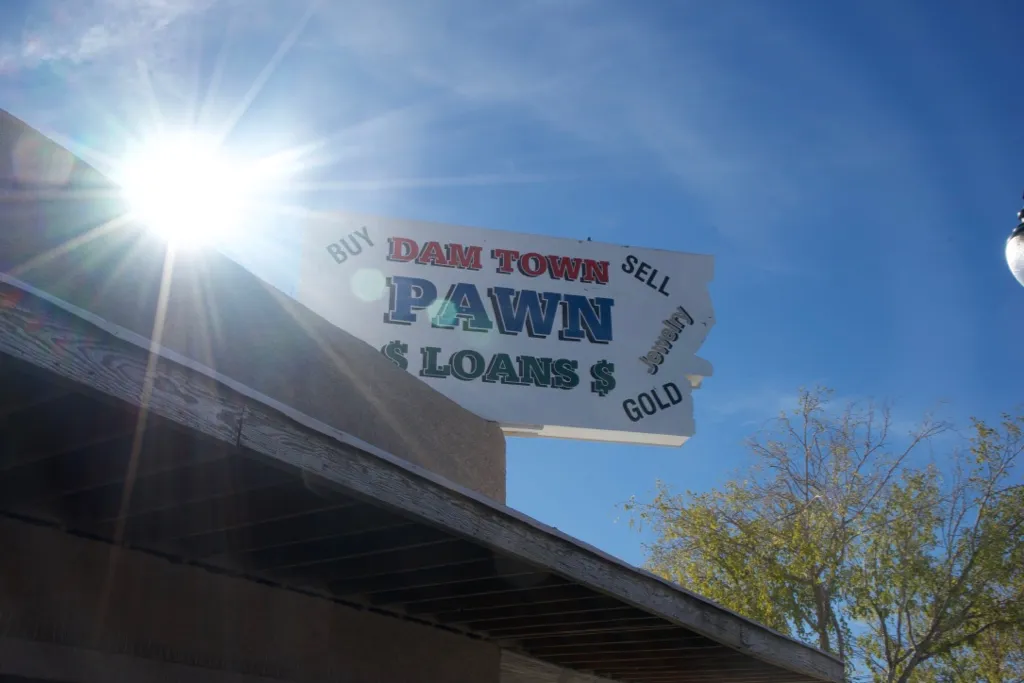 A painted sign reading Dam Town Pawn, Buy Sell, Loans, Gold, against a bright sky.