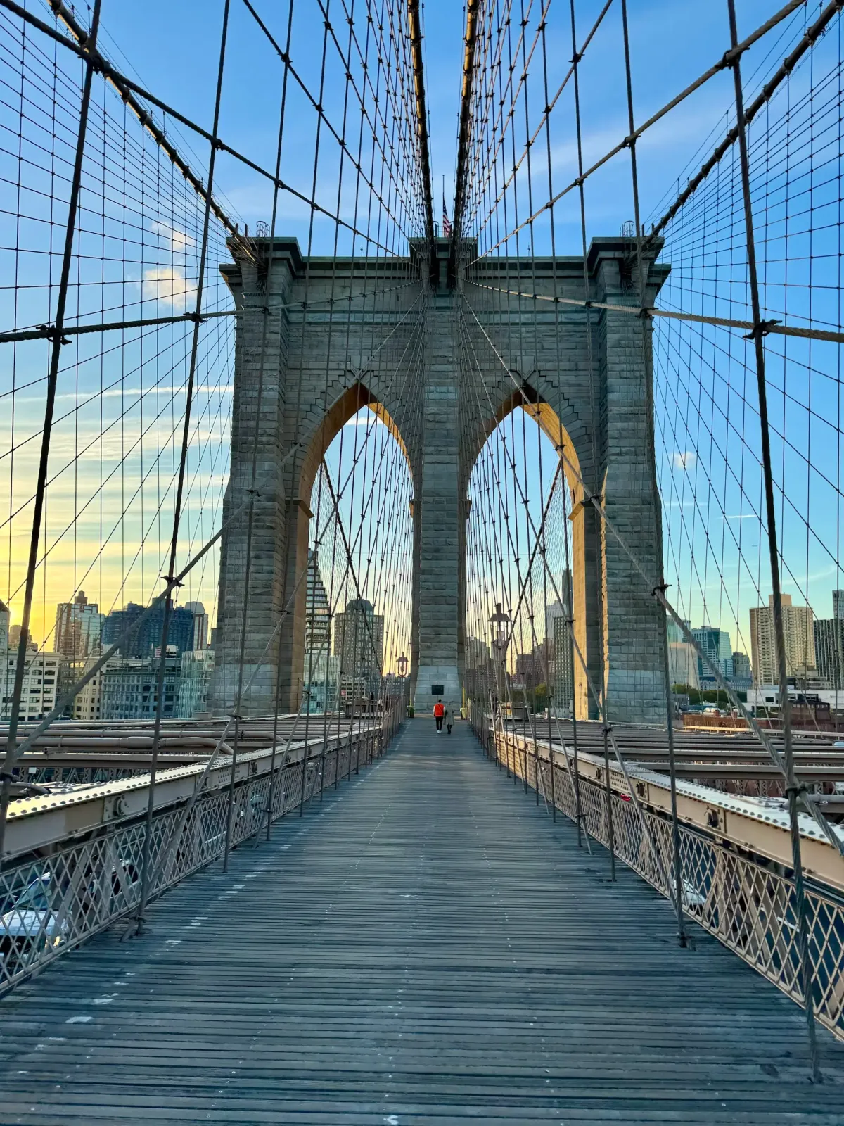 The walkway of the Brooklyn Bridge leading to one of its stone towers, framed by suspension cables.
