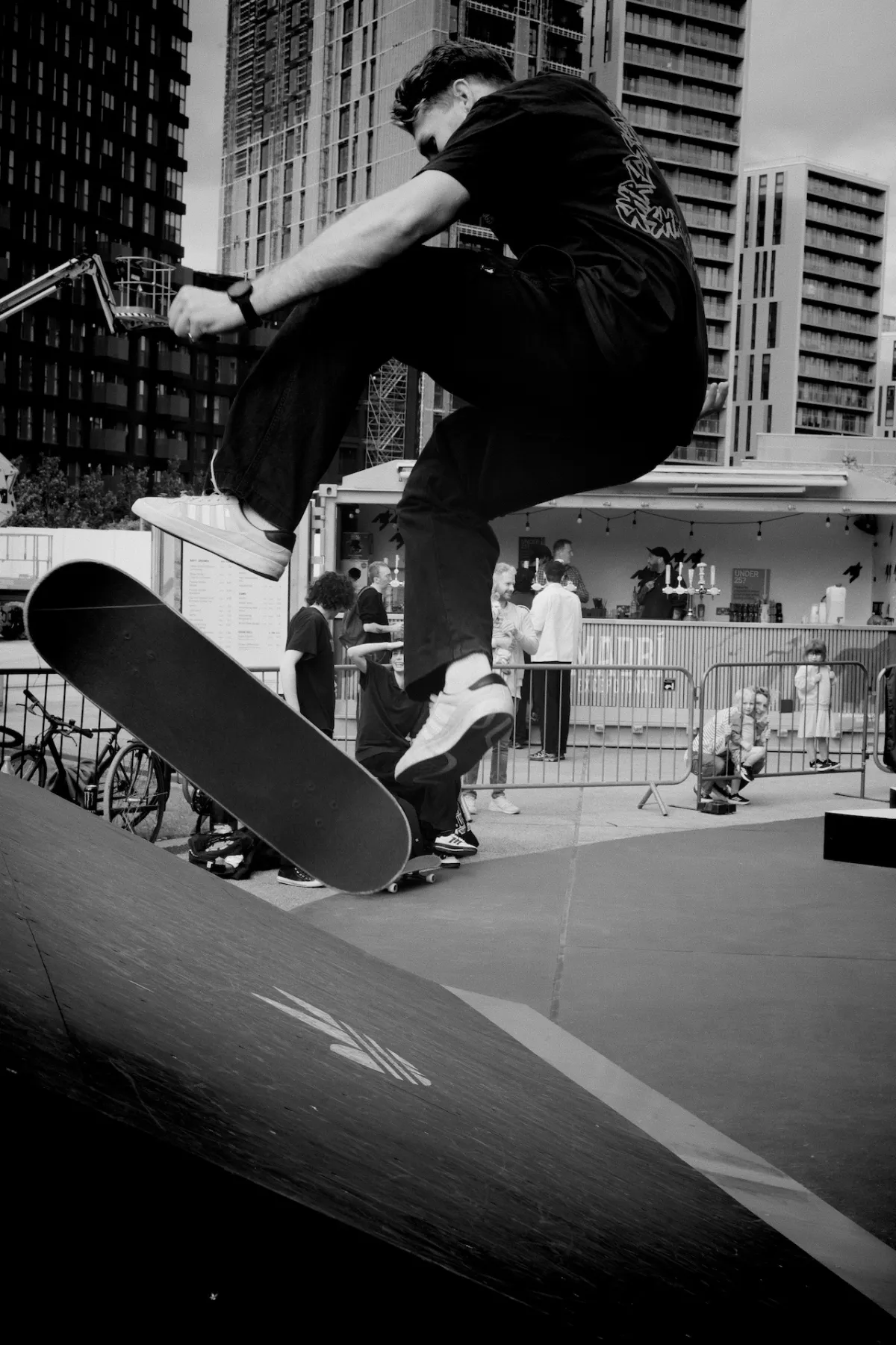 A skateboarder in mid-air above a ramp, with tower blocks behind. Black and white.