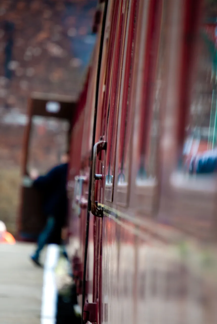 The side of a maroon railway carriage in close-up, with a figure walking beyond.