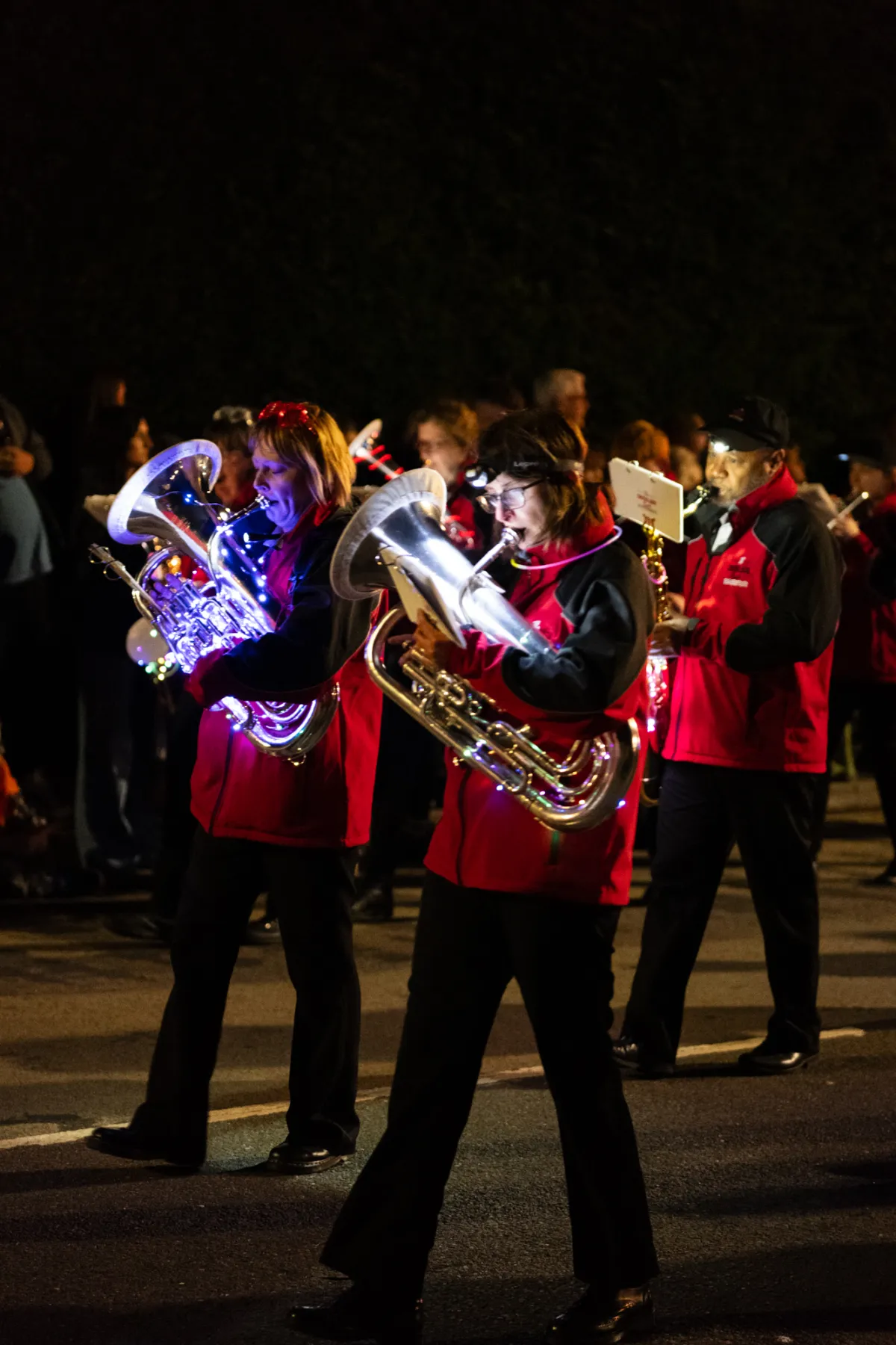 A marching band in red jackets playing brass instruments at night.