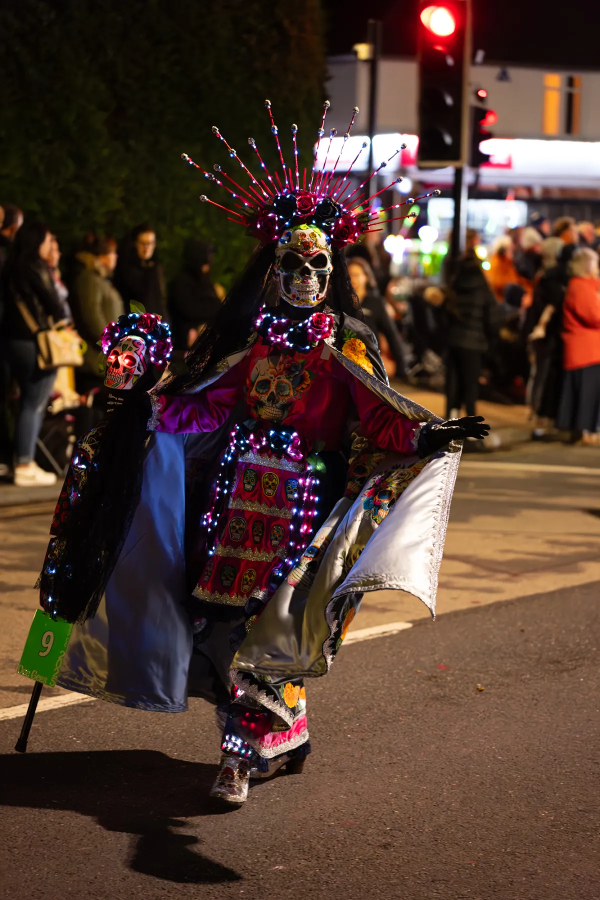 A performer in a skeleton mask and beaded headdress walking the parade route.