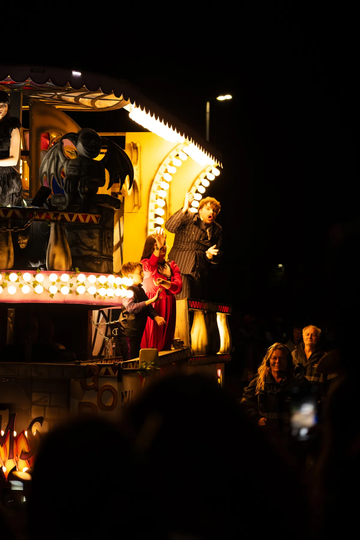 Performers on a lit float, one waving from an upper deck.