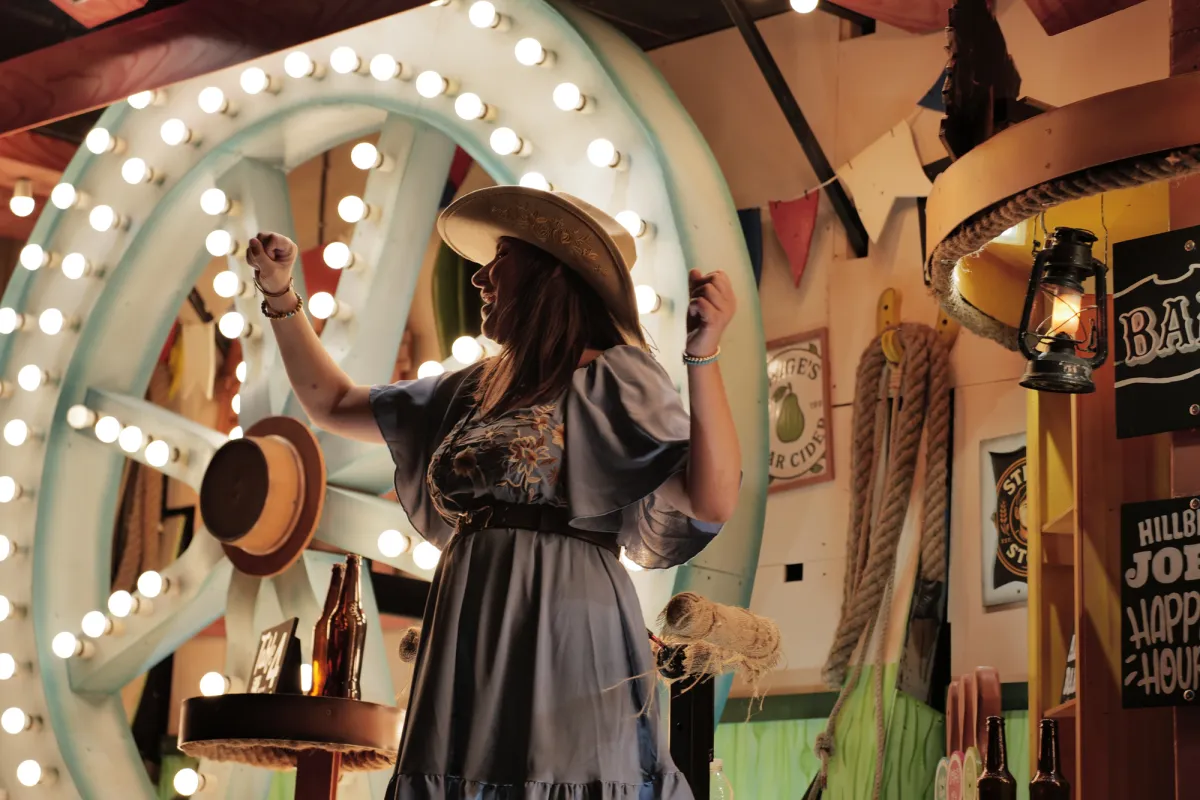 A performer in a straw hat dancing in front of a light-studded wagon wheel.
