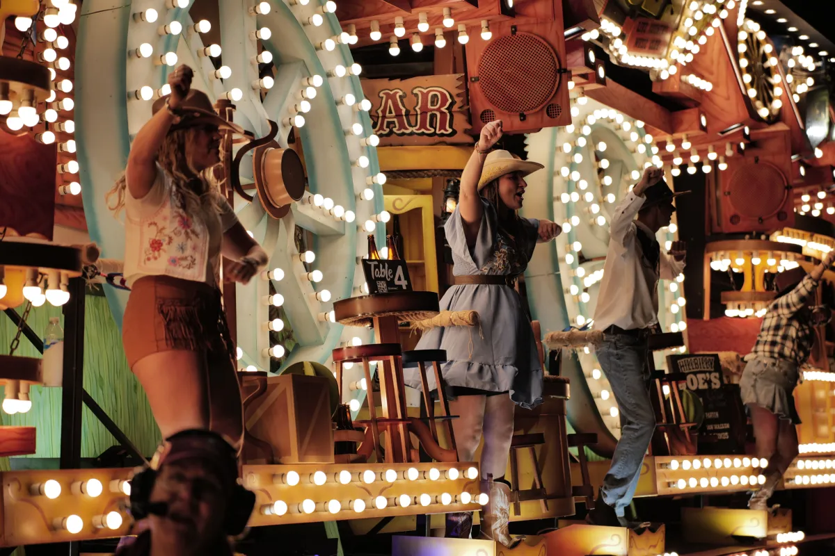 Performers in western costume dancing among light bulbs and painted scenery.