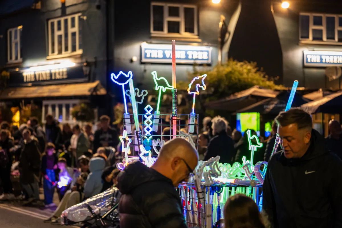 A street vendor's stall of illuminated neon toys, with a pub behind.