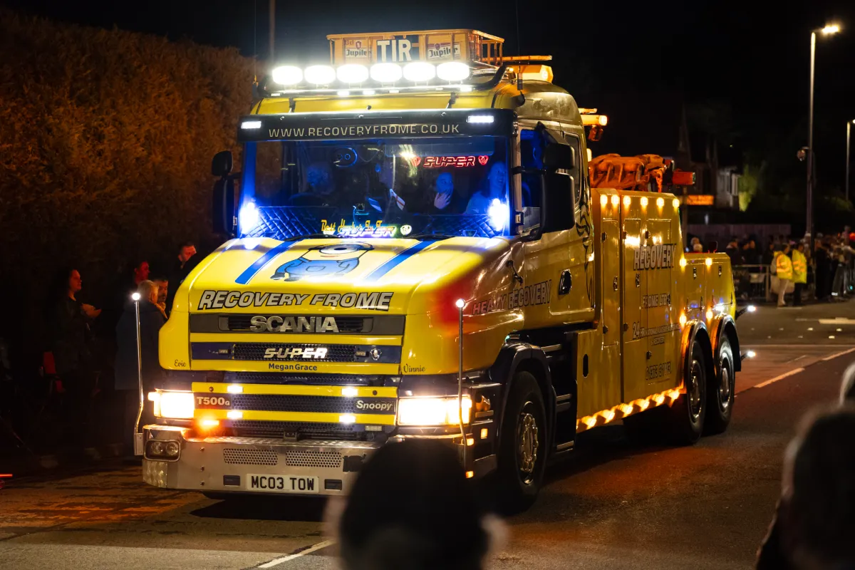 A yellow Scania recovery truck lit up at night, lettered Recovery Frome.