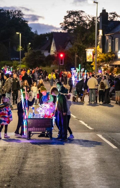 A crowd lining a street at night, waiting for a carnival procession to pass.