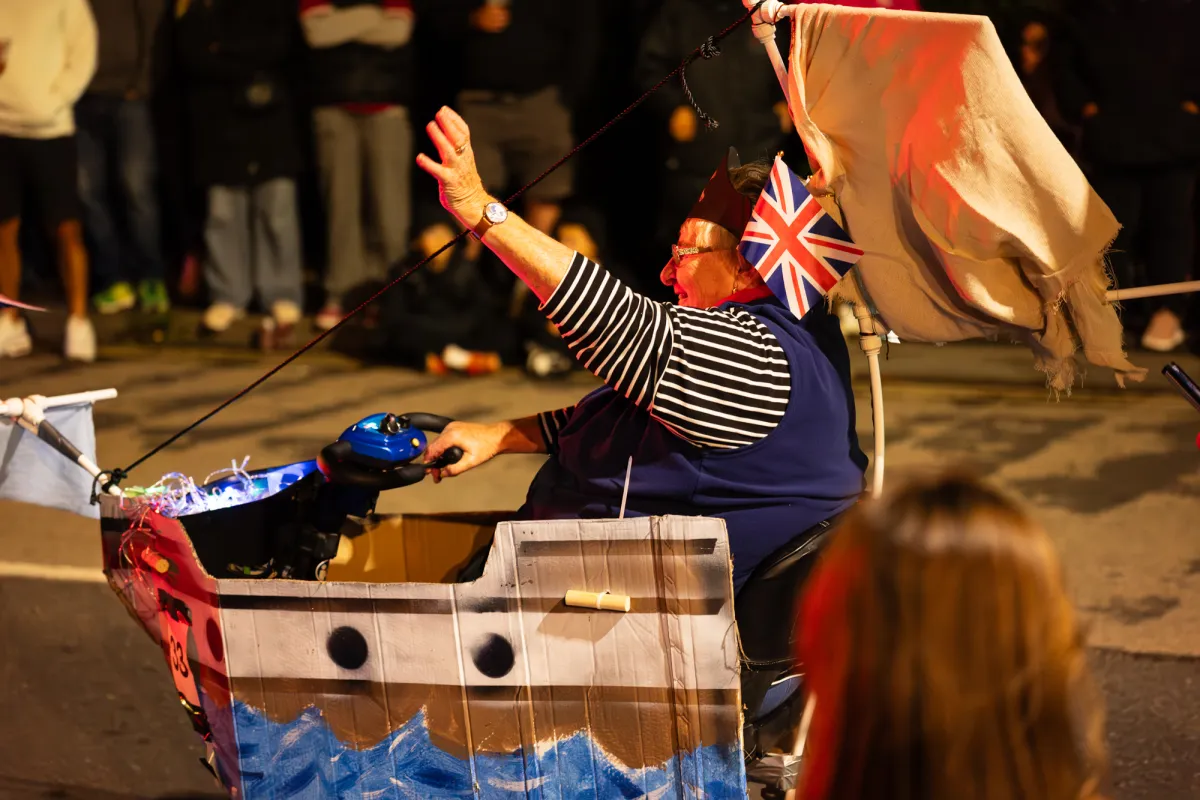 A person in a cardboard boat costume waving a Union flag.