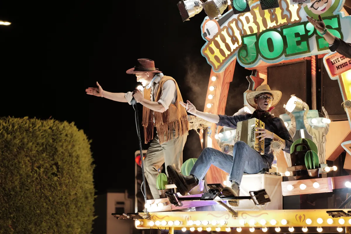 Two performers in cowboy costume on a brightly lit float.