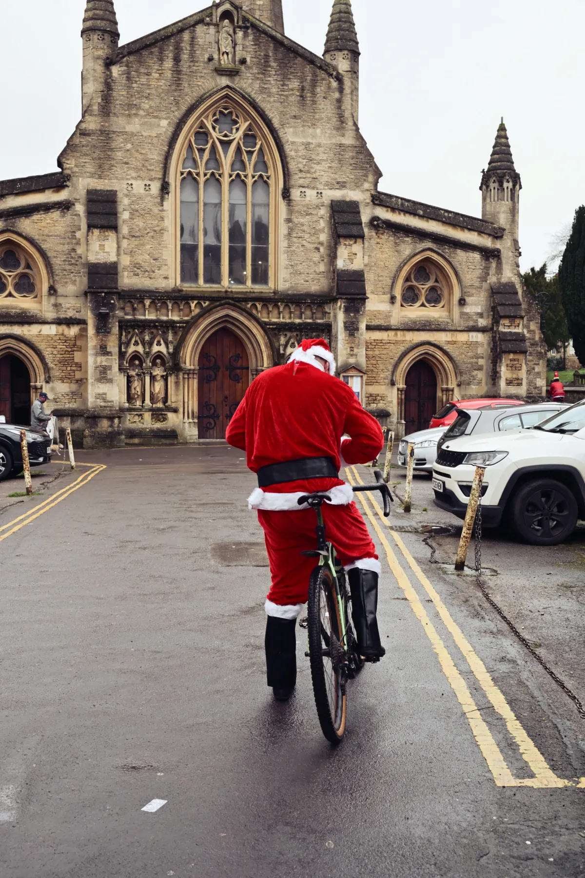 A cyclist in a Father Christmas suit riding past a stone church.