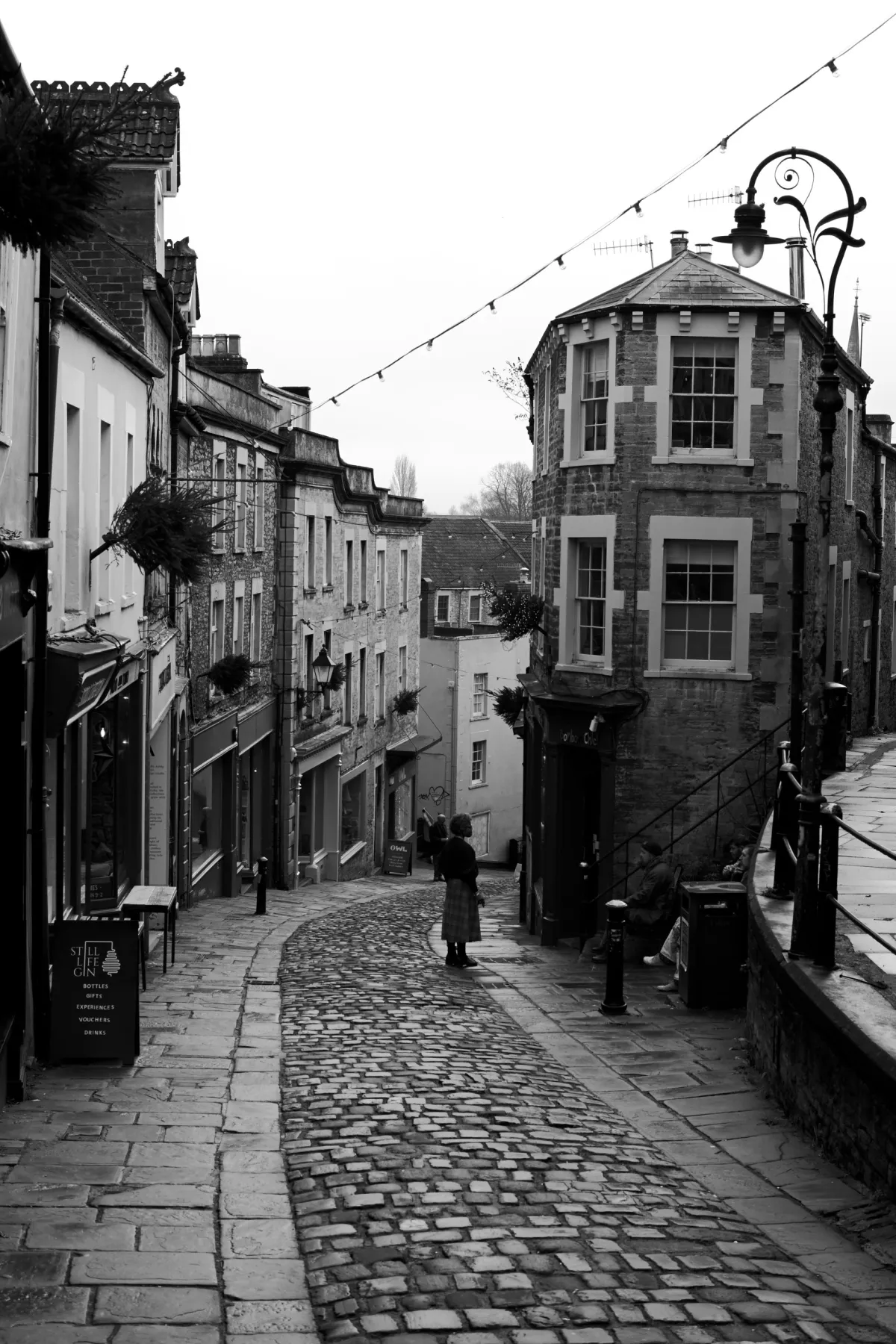 A cobbled street curving past a stone corner building. Black and white.