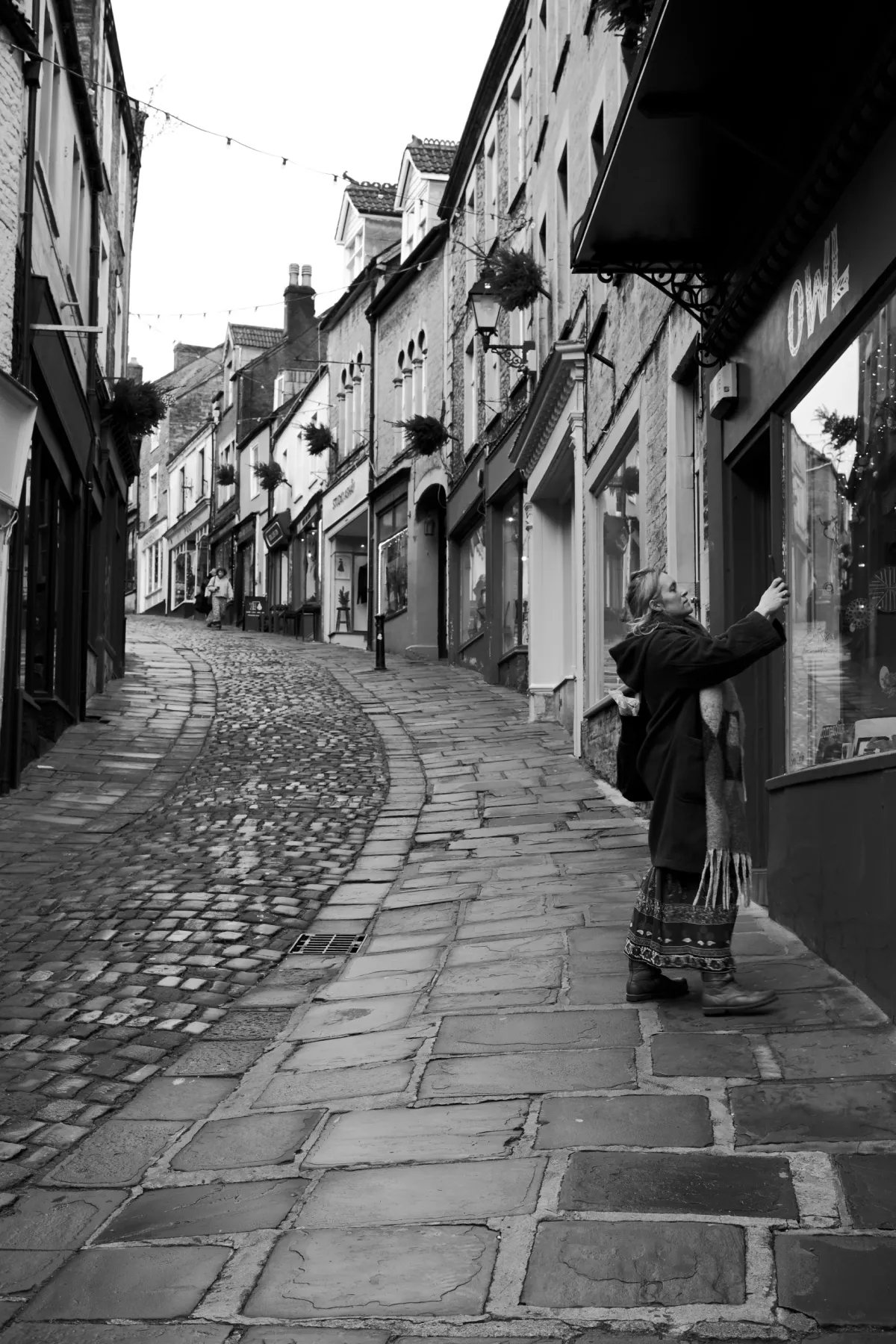 A woman looking into a shop window on a steep cobbled street. Black and white.
