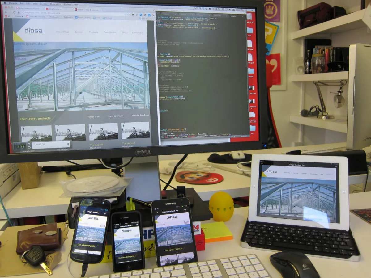 A desk with a website design shown at once on a monitor, a tablet and three phones.