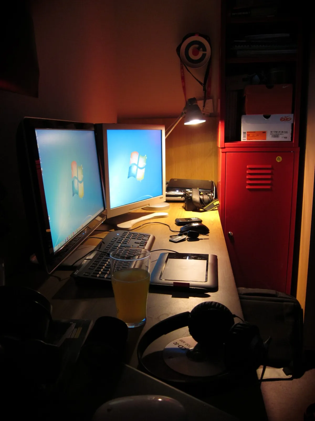 A home desk at night with two monitors, a keyboard and a graphics tablet, lit by an angled lamp.