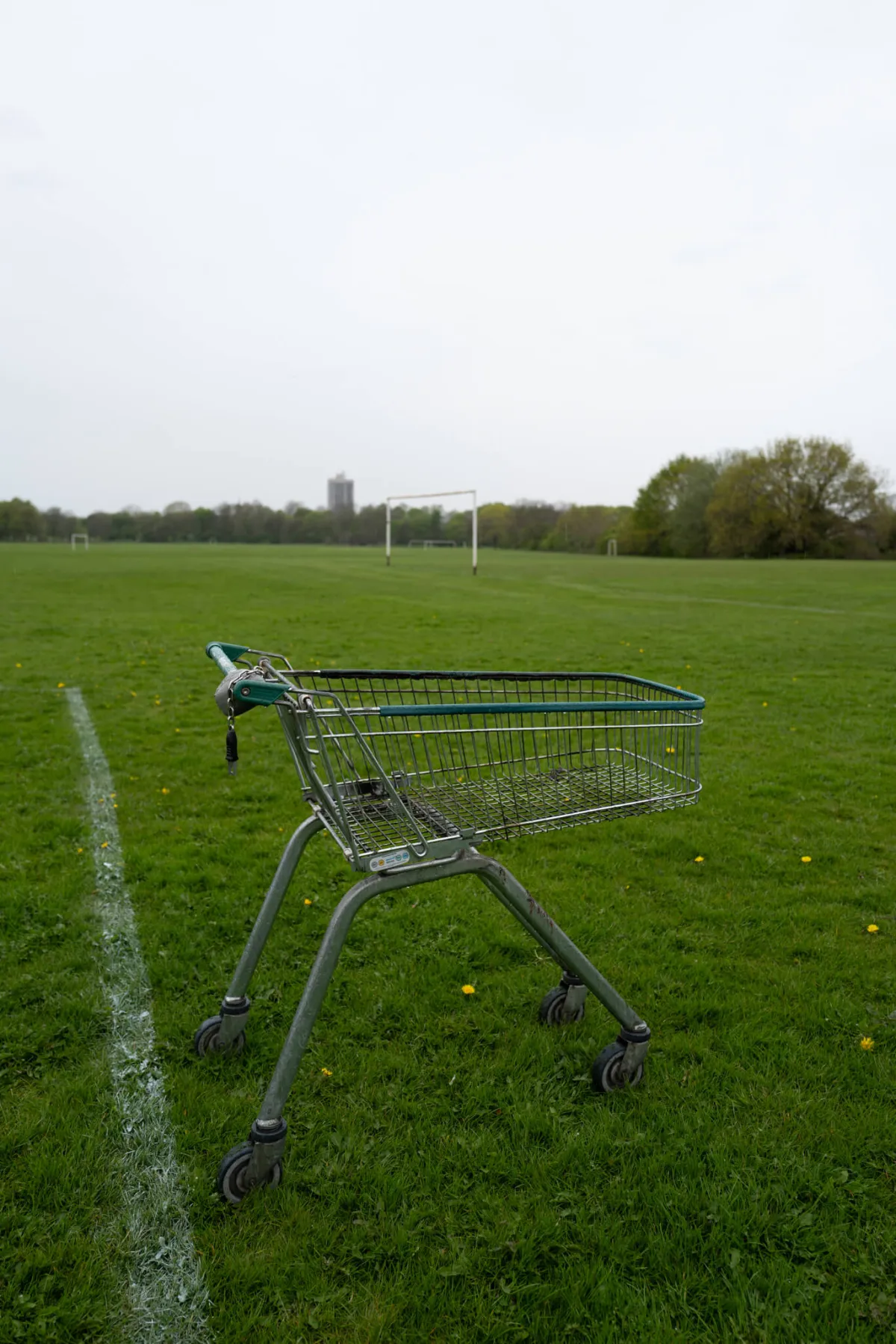 An abandoned shopping trolley on a playing field, with goalposts behind.