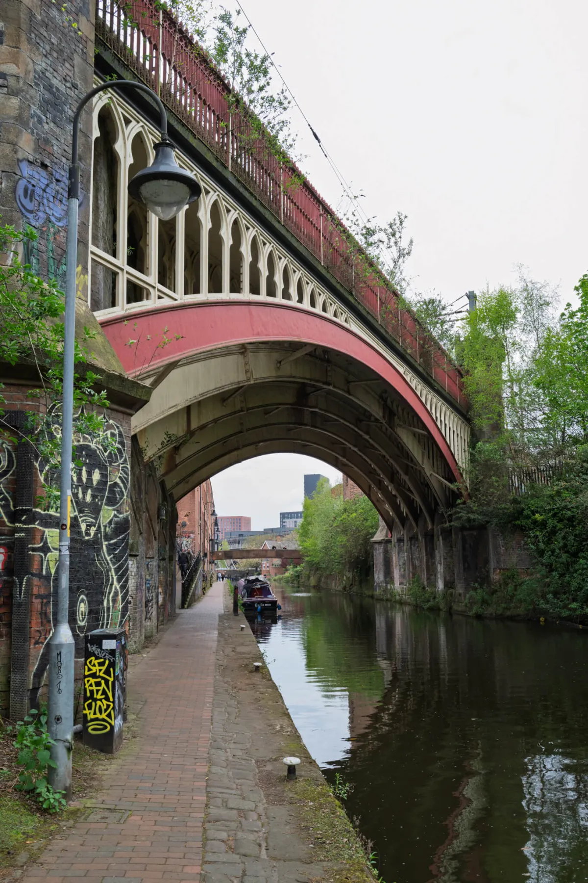 A red iron bridge crossing a canal, with a graffitied towpath beneath.