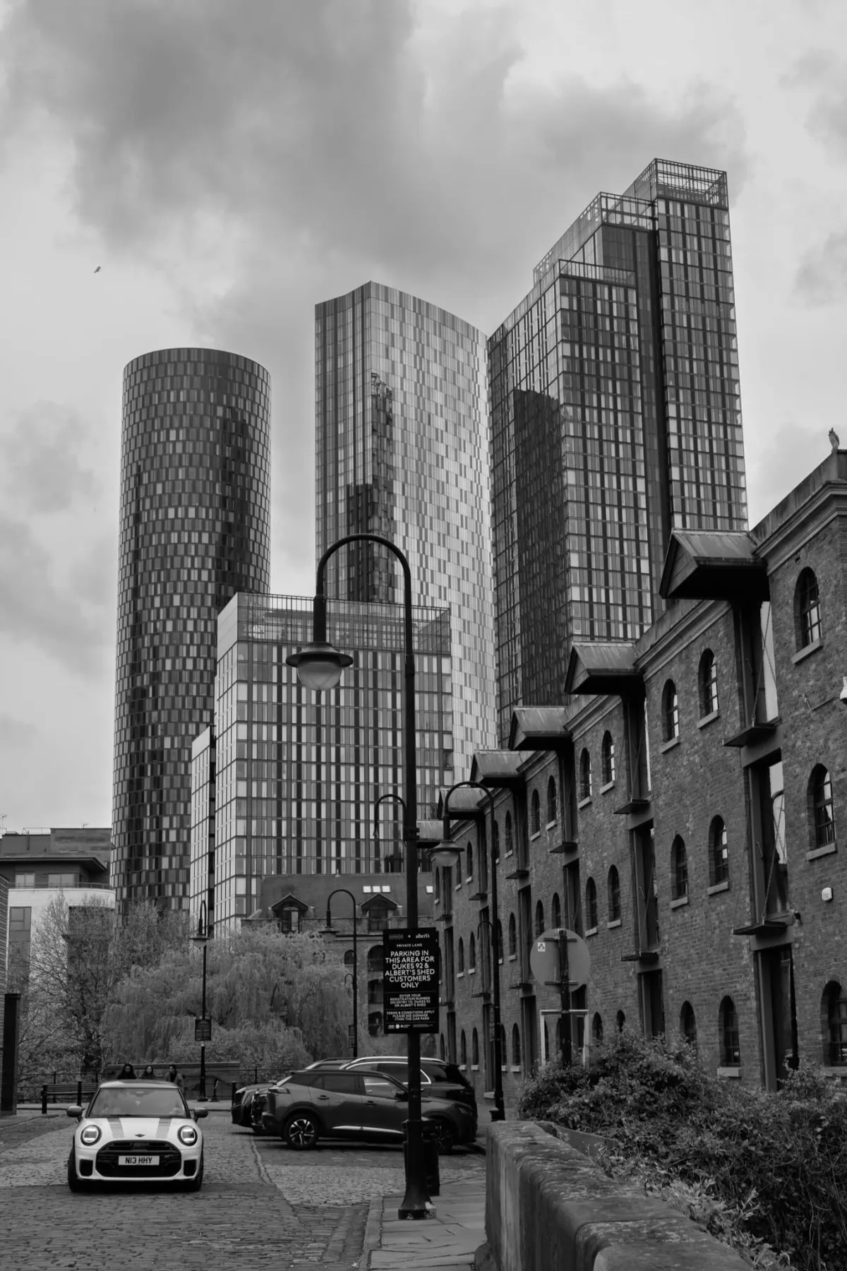 Tall glass towers above a terrace of brick warehouses. Black and white.