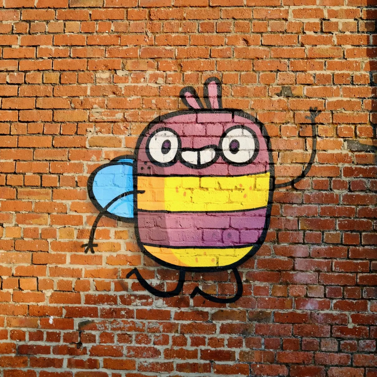A cartoon bee character painted on a red brick wall.