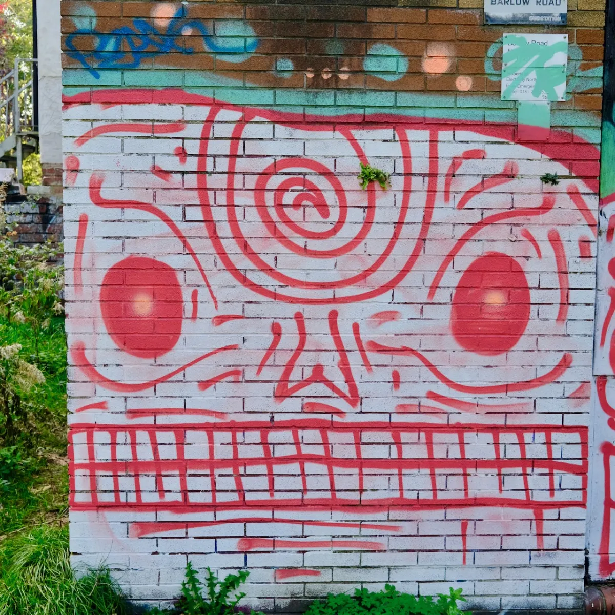 A large red line-drawn face painted across a whitewashed brick wall.
