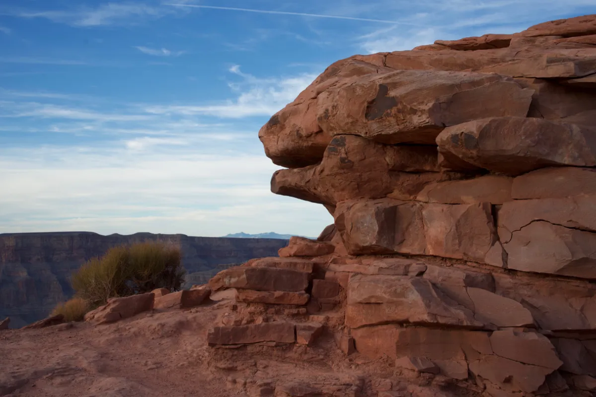Layered red sandstone at the canyon rim, with the far wall in the distance.