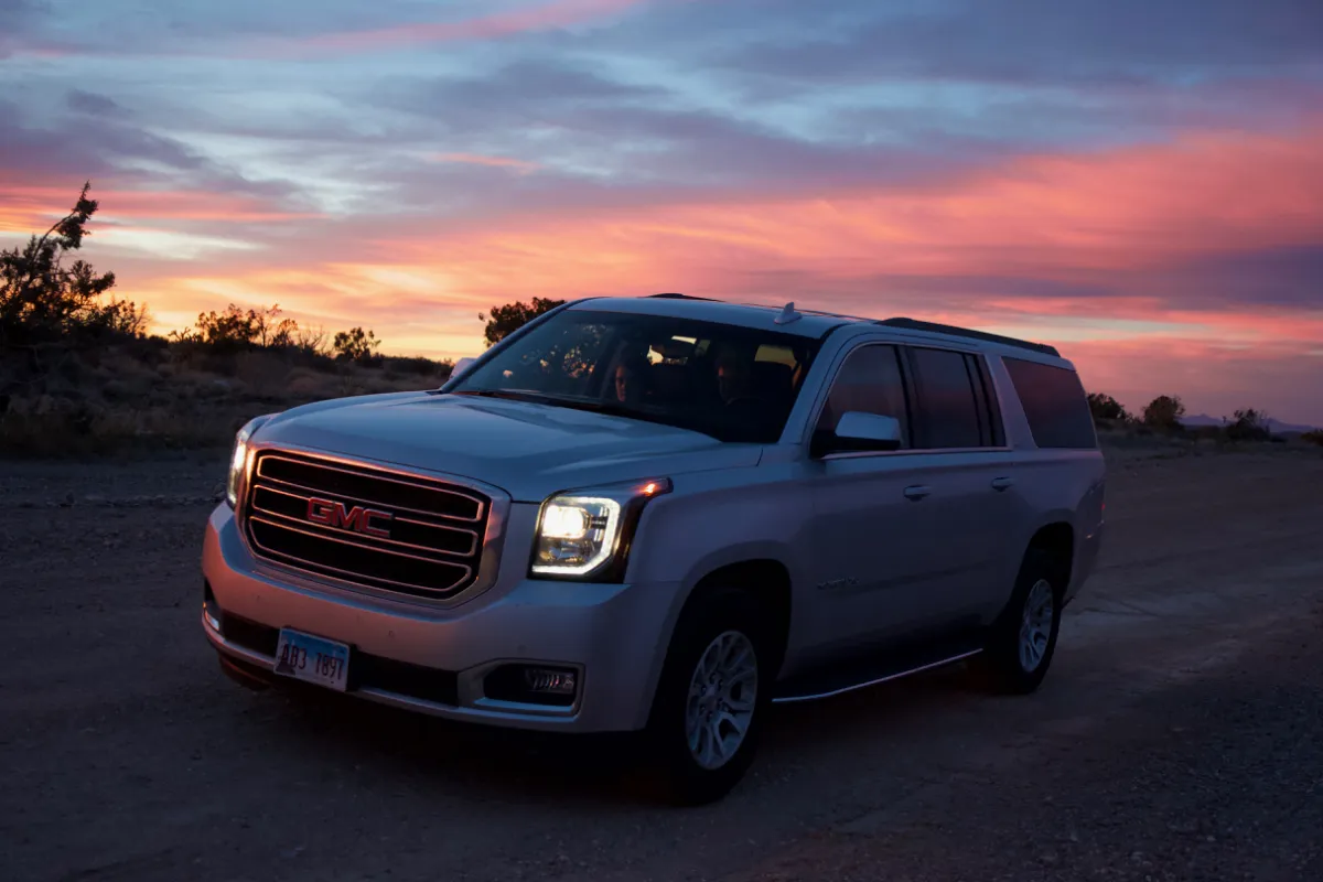 A silver GMC people carrier parked on a desert track at sunset.