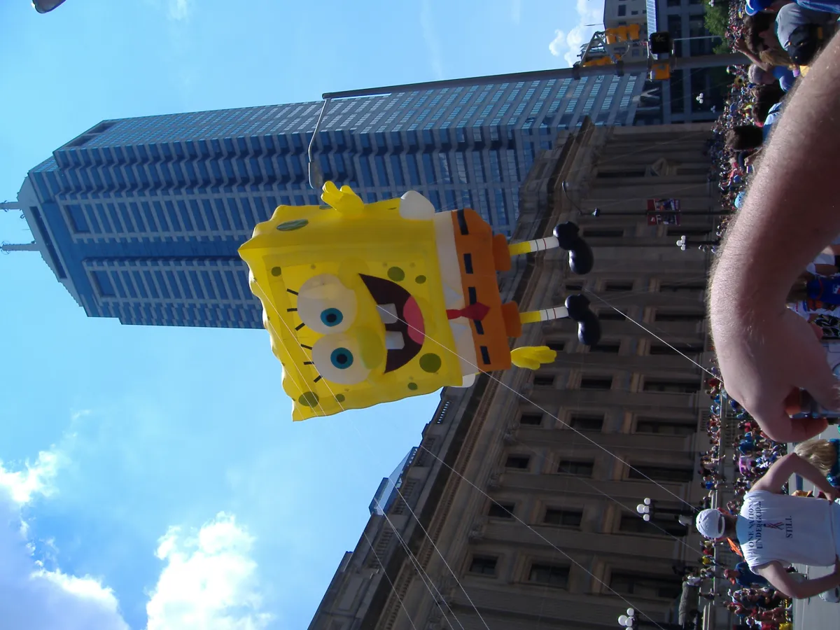 A SpongeBob SquarePants parade balloon passing between office towers.