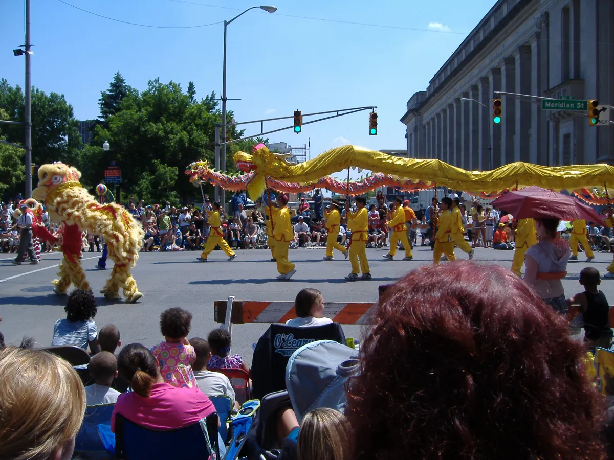 Performers in yellow costumes carrying a Chinese dragon along a street during a parade.