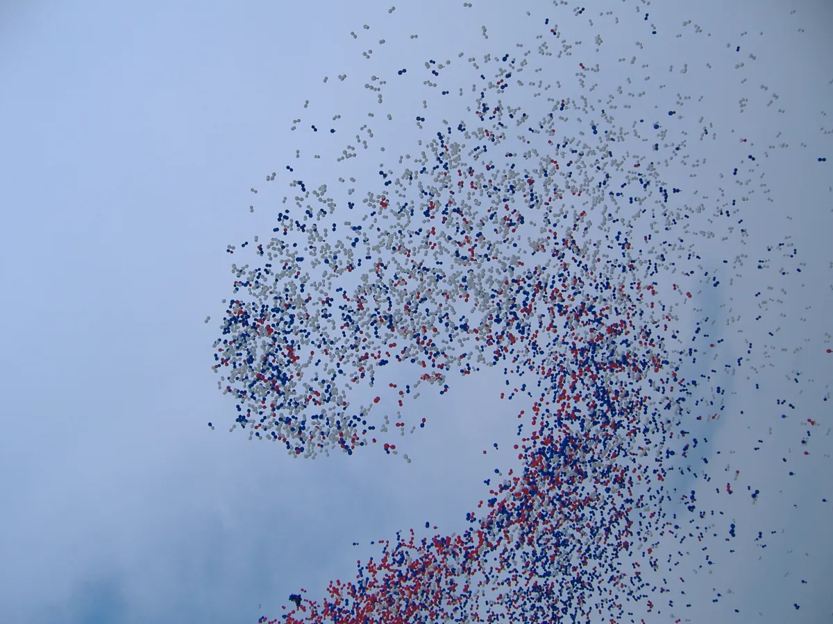 Thousands of red, white and blue balloons released into an overcast sky.
