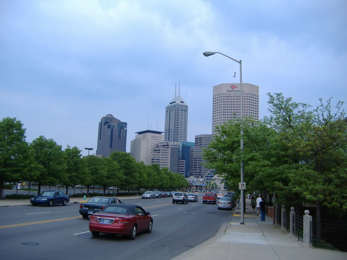 A city street lined with trees, with the downtown Indianapolis skyline ahead.