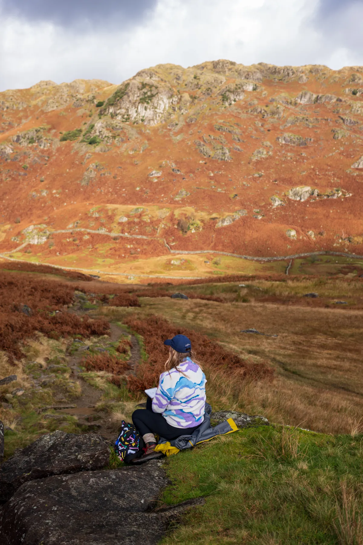 A walker following a stream along a broad valley floor covered in bracken.