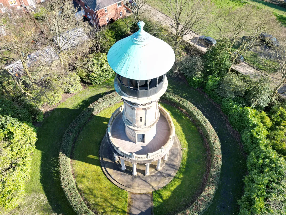 An aerial view of a stone tower with a green domed roof, ringed by hedges.