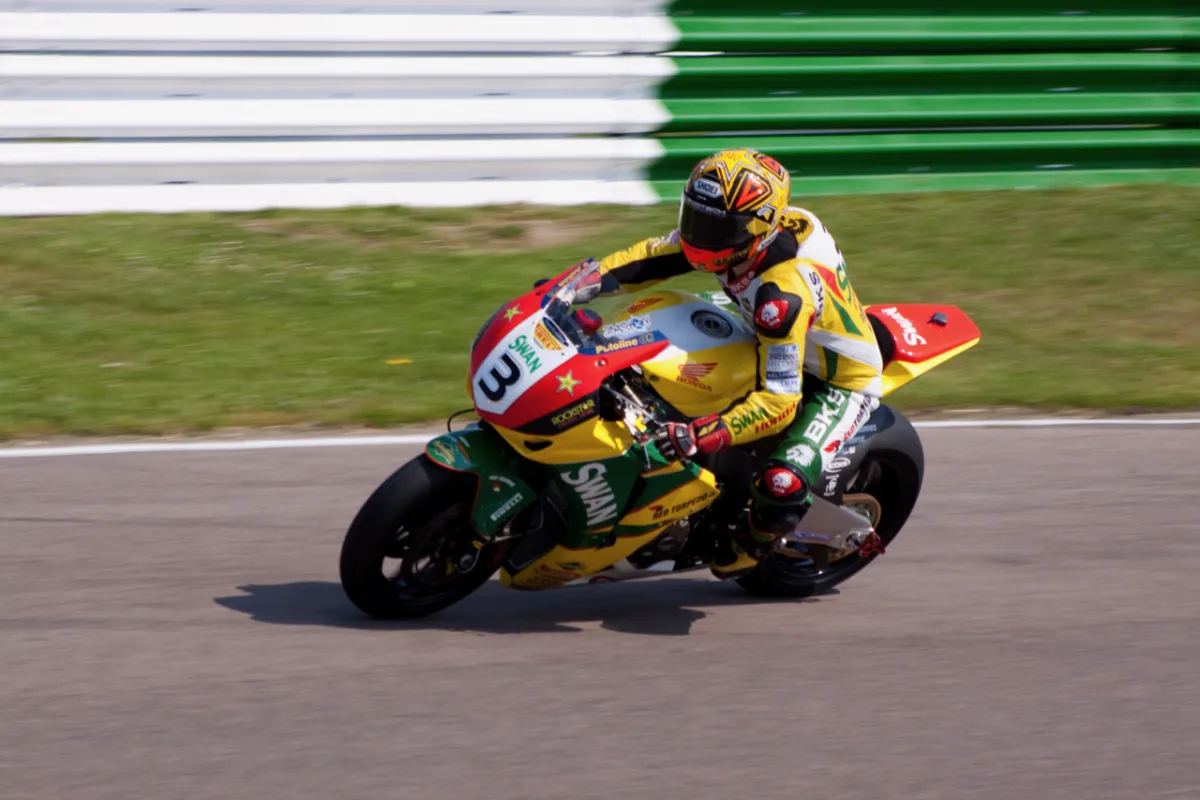 A rider on a green and yellow racing motorcycle cornering on a track.