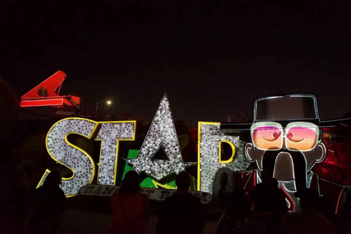A large illuminated sign spelling STAR at night, beside a painted figure in sunglasses and a hat.