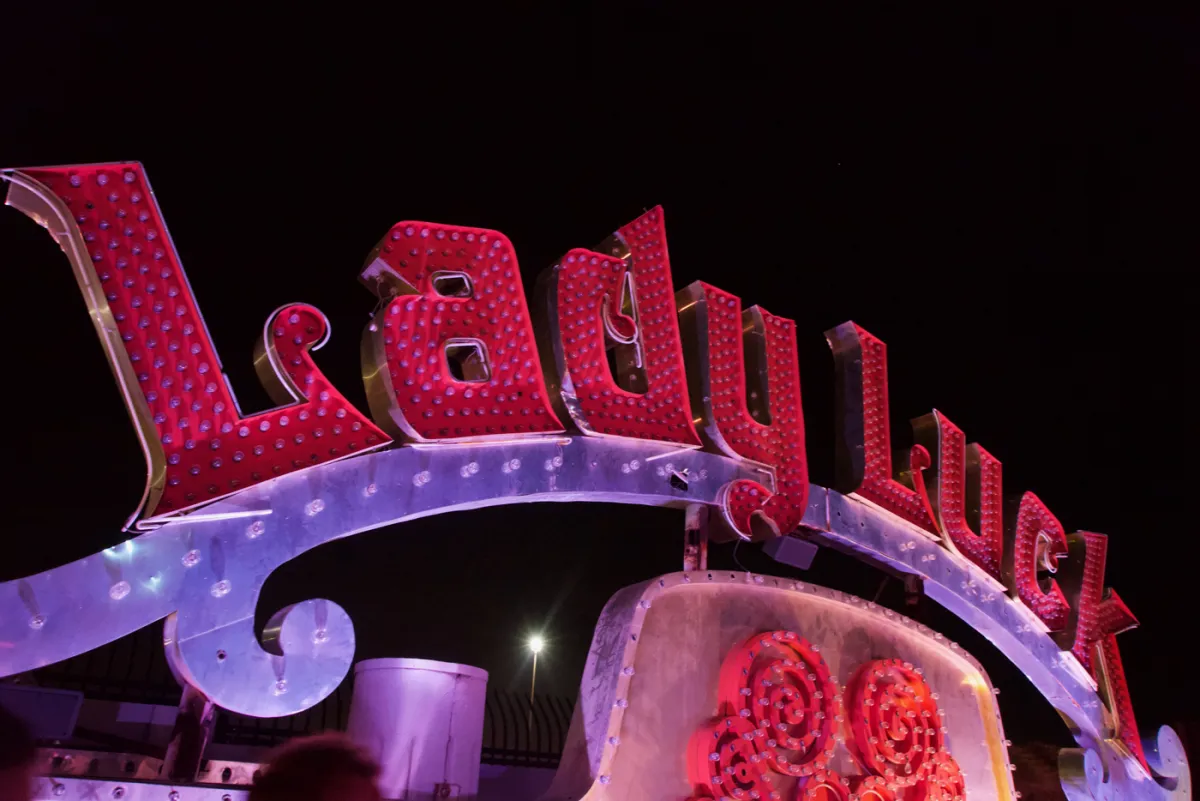A red neon sign reading Lady Luck mounted on a curved metal frame at night.